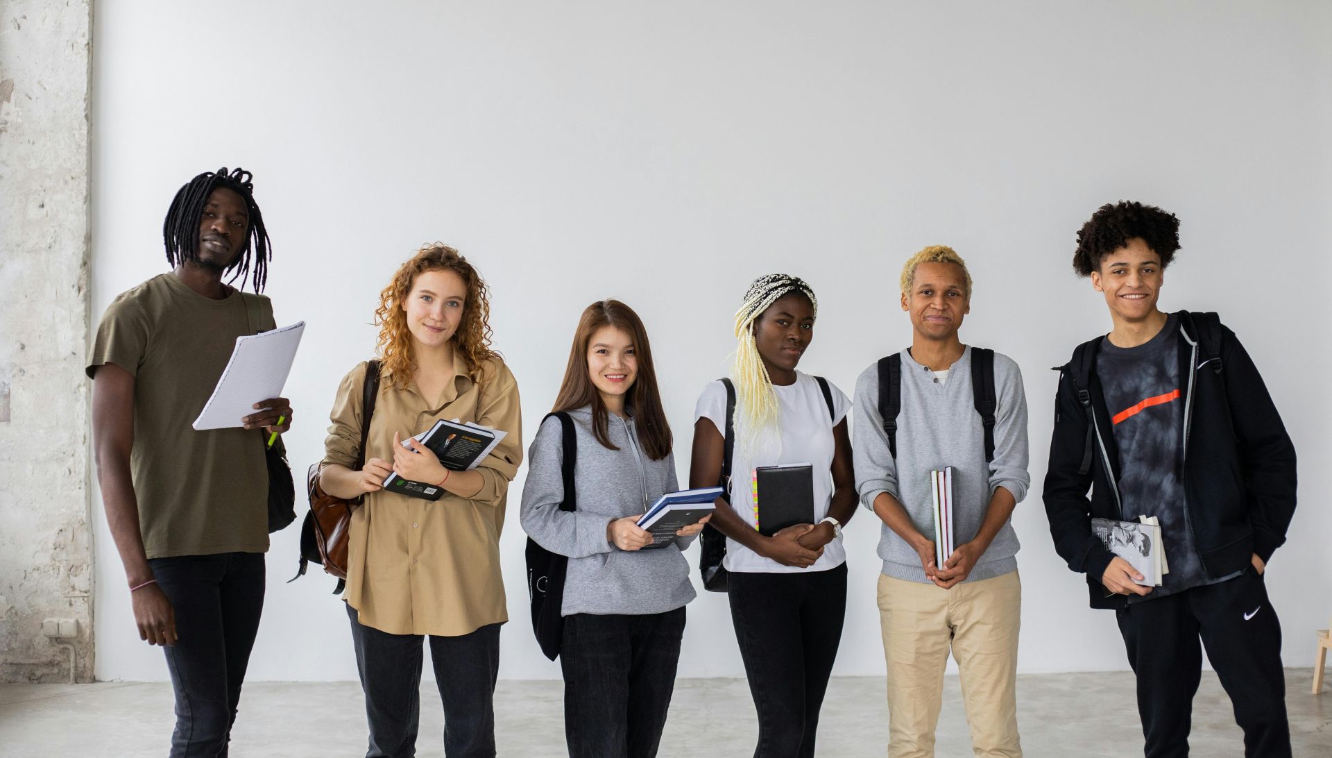 Group of diverse young multiracial classmates with notebooks and textbooks and backpacks smiling at camera