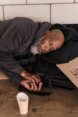 Bald African American man resting on the pavement, depicting homelessness and poverty.